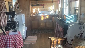 A cozy cabin interior with a wooden ceiling, a dining area with a checkered tablecloth, a kitchen with a sink and stove, and a window with plaid curtains. - Brand new tiny cabin located on farm. Near rivers, trailsheads & national forest (West Plains)