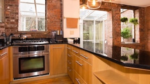 A modern kitchen with a brick wall, stainless steel appliances, wooden cabinets, and a large window. - Garden Level Suite, Court Street (New Haven)