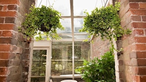 A cozy corner with a brick wall, a glass door leading outside, and two hanging planters with lush green plants. - Garden Level Suite, Court Street (New Haven)