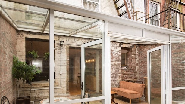 A glass-enclosed patio with a brick wall, a wooden table, a cushioned bench, and a potted plant. - Garden Level Suite, Court Street (New Haven)