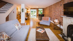 A spacious living area with a sofa, coffee table, and fireplace. A staircase leads to an upper level. - Garden Level Suite, Court Street (New Haven)
