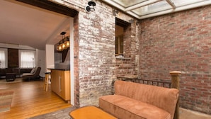 A cozy living room with a brick wall, a sofa, a small table, and a glass ceiling. - Garden Level Suite, Court Street (New Haven)