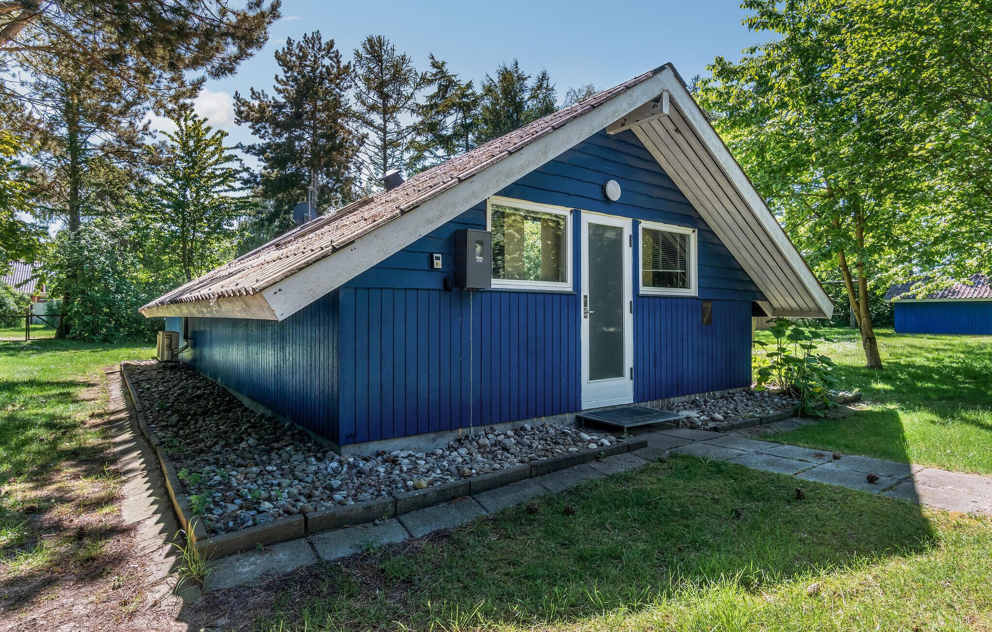 Una casa pequeña de un solo piso, azul, con techo inclinado, una puerta principal y una ventana.