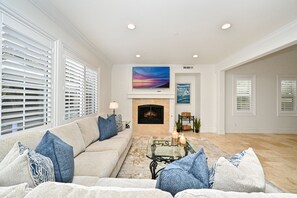 A living room with a beige sofa, a fireplace, a TV, and artwork on the wall. - Large Home in Gated Community near Monarch Beach with Jacuzzi (Dana Point)