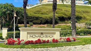 Señal de Monarch Beach, con una zona ajardinada que incluye palmeras y flores rojas.