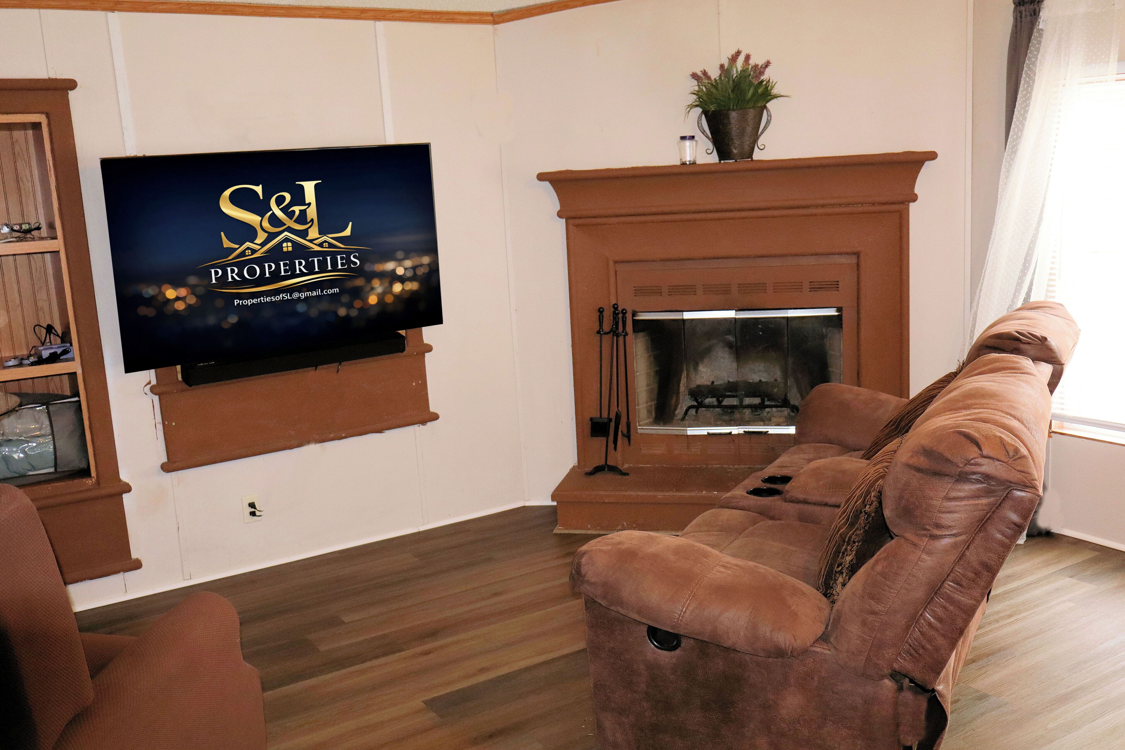 Un saló amb una televisió que mostra 'S&L Properties', una llar de foc i un sofà de cuir marró.