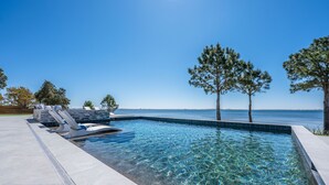 A clear swimming pool with lounge chairs and trees in the background.