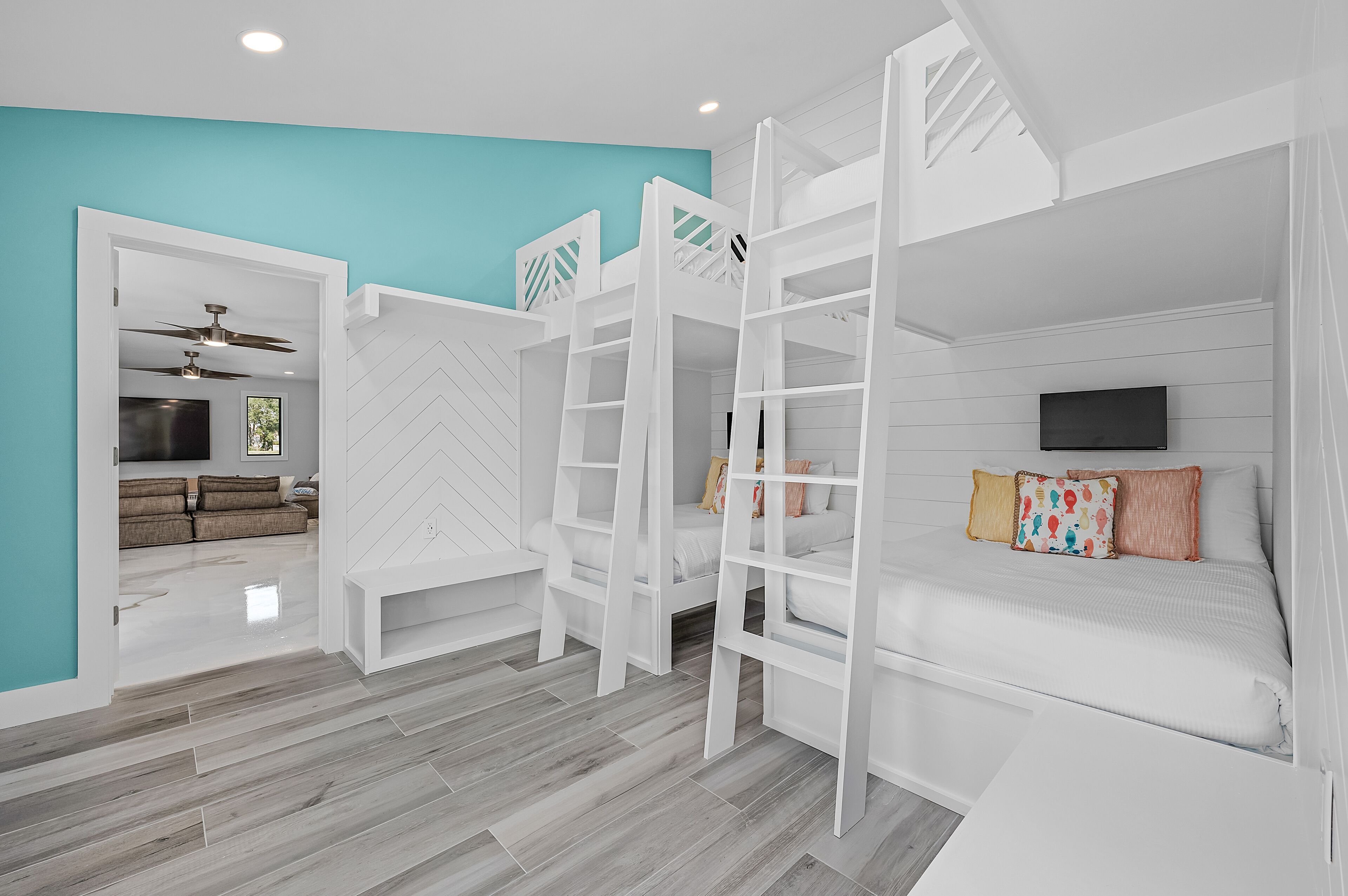 A room with a bunk bed, a ceiling fan, a TV, and a view into another room with a sofa and a ceiling fan.