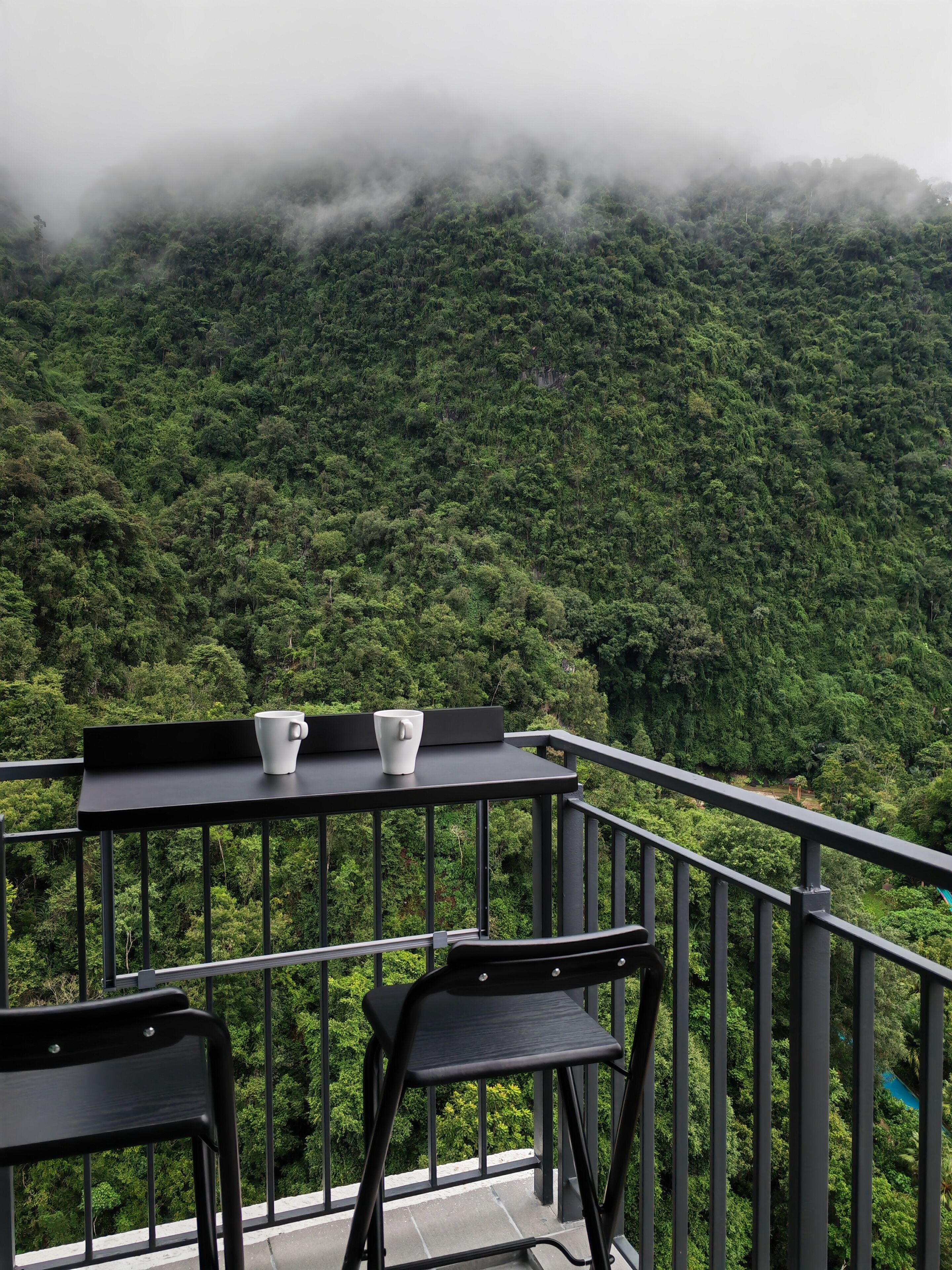 Un balcon avec une table et des chaises donnant sur une montagne verdoyante et couverte de forêts.