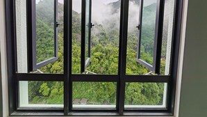 Una ventana con vistas a un bosque verde y exuberante y montañas cubiertas de bruma.