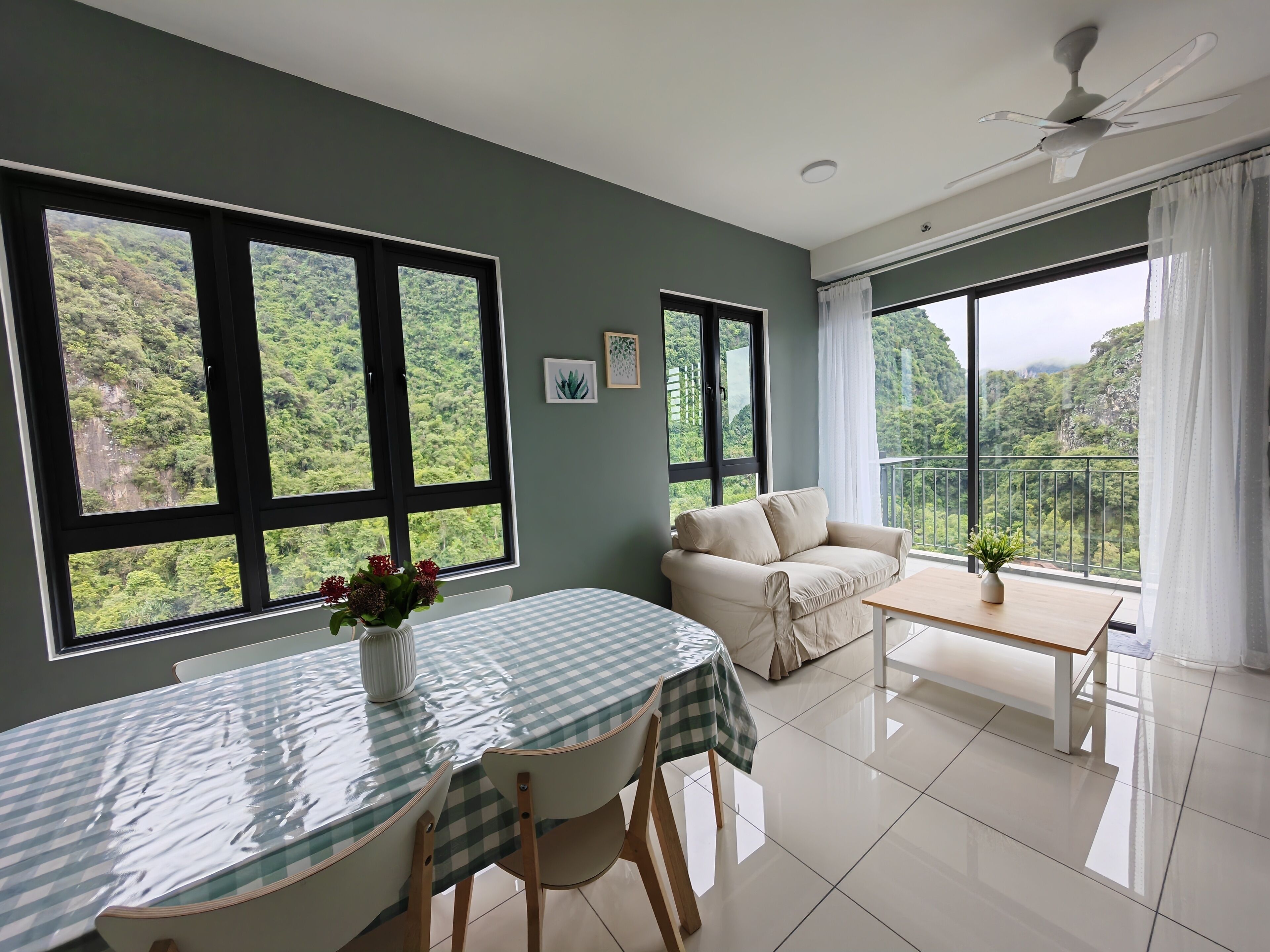 A room with a dining table, a sofa, and large windows offering a view of a forested area.