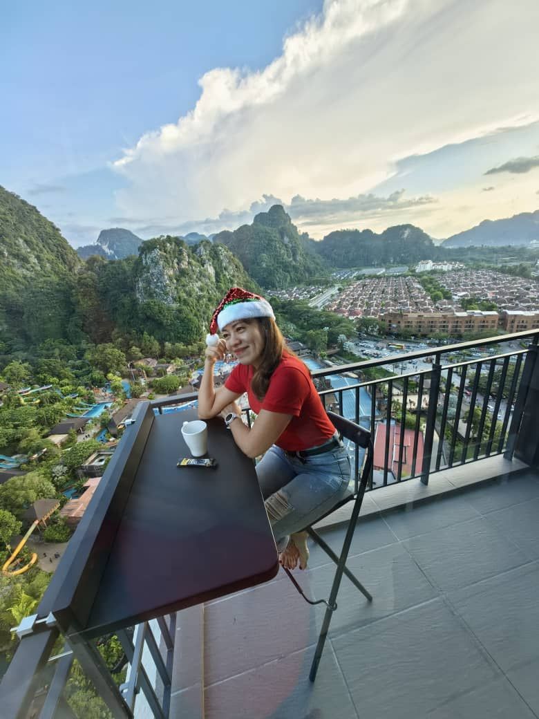 A person seated at a table on a balcony with a view of a mountainous landscape and a city below.