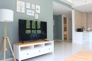A modern living room with a flat-screen TV on a wooden stand, a white entertainment unit, and framed botanical prints on the wall.