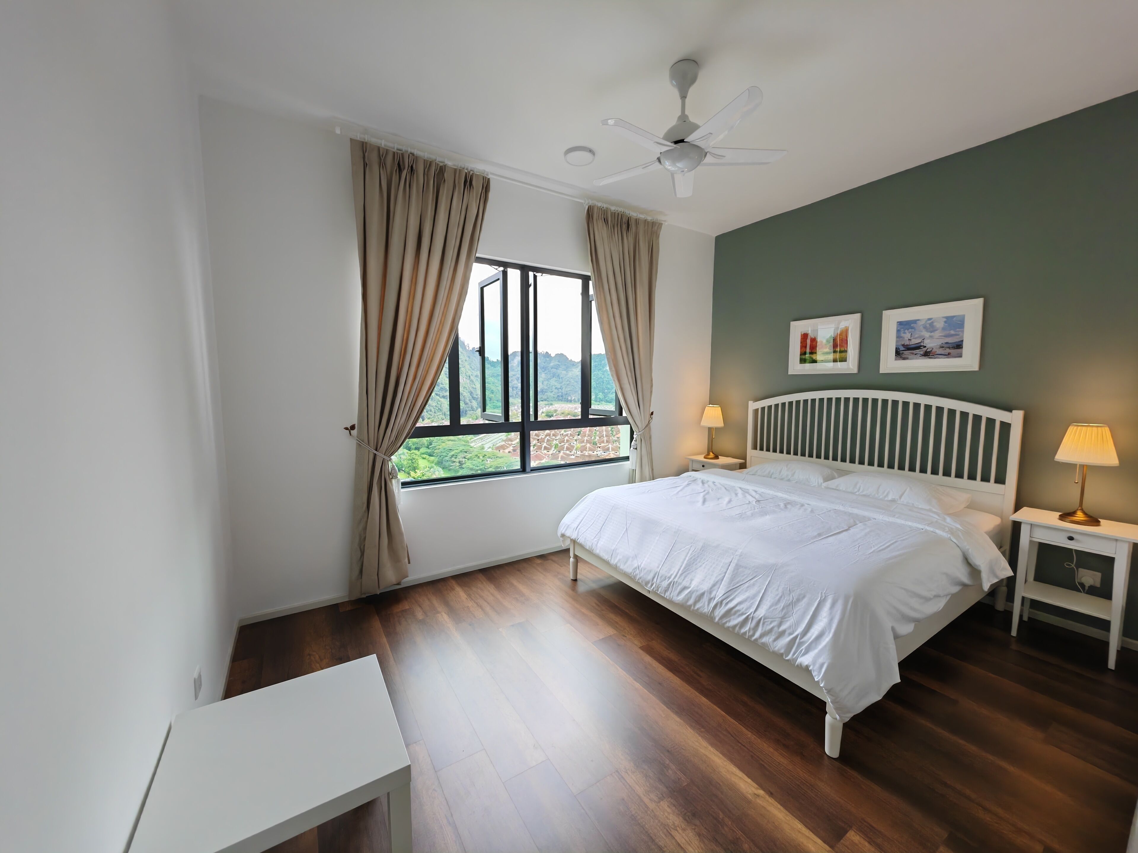 A bedroom with a bed, bedside tables, a ceiling fan, a window with curtains, and artwork on the wall.