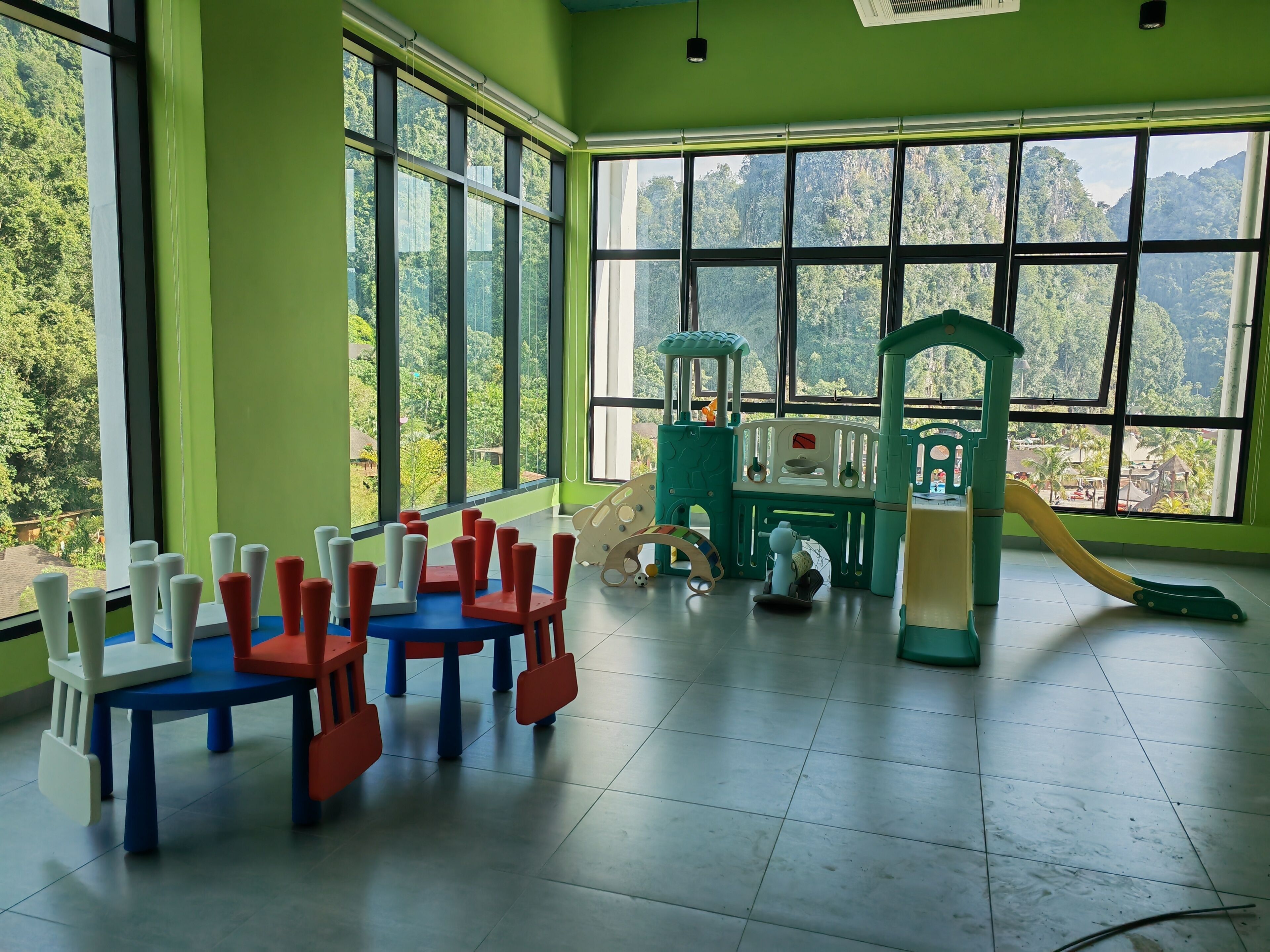 Ein Zimmer mit großen Fenstern, ein Spielbereich mit einer Rutsche und mehrere Stühle.