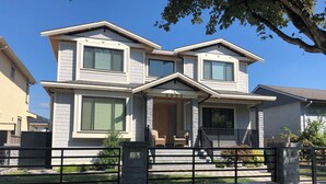 A two-story house with a stone facade, large windows, and a front porch with outdoor seating. - Beautiful 5 star 2 bd suite near bus&shopping (Burnaby)