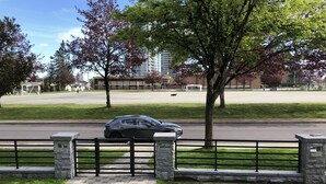A paved pathway leading to a gated area with stone pillars, a grassy field, and a building in the background. - Beautiful 5 star 2 bd suite near bus&shopping (Burnaby)