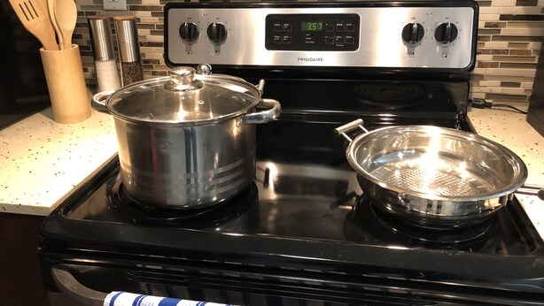A kitchen with a stainless steel stove, a pot on the left burner, and a pan on the right. There are wooden utensils in a holder and a spice rack on the counter. - Beautiful 5 star 2 bd suite near bus&shopping (Burnaby)