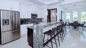 A modern kitchen with stainless steel appliances, a marble countertop, and a bar area with stools.