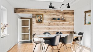 A dining area with a wooden wall, a painting, and a window with flowers. - 3 bedroom nice home in Thyborøn (Thyborøn)