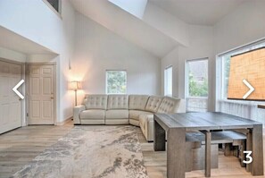 A spacious living room with a large sectional sofa, a wooden coffee table, and a view of the outdoors through large windows.