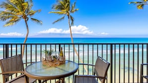 A balcony with a glass table and chairs, overlooking a beach with palm trees and the ocean. - Stunning oceanfront view with Maui-inspired design (Lahaina)