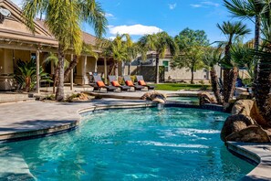 Une piscine avec des chaises longues, des palmiers et un patio couvert.