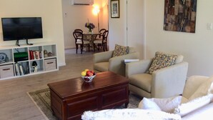 A living room with a TV, sofa, coffee table, and a dining area in the background.