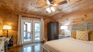 Une chambre dans une cabane en bois, comprenant un lit, un bureau, une chaise, une armoire et un ventilateur de plafond.