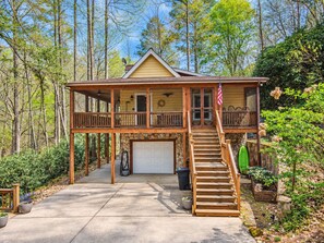 A two-story wooden cabin with a balcony, a garage, and a staircase leading to the upper level.