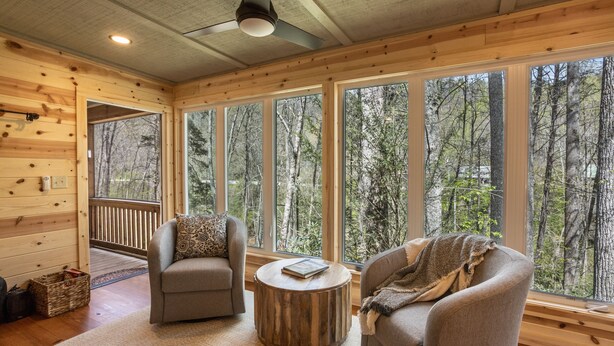 L’intérieur chaleureux d’un chalet avec deux canapés, une table basse ronde en bois et de grandes fenêtres donnant sur la forêt.