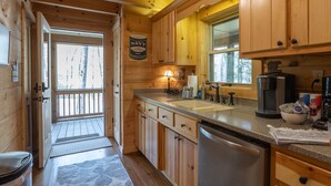 Une cuisine rustique aménagée dans une cabane en bois, avec une porte en bois, une machine à café et un évier.