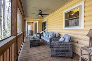 A wooden deck with wicker furniture, a ceiling fan, and a large window. - The TrainStation | Secluded Cabin with Large Deck, Waterfall, & Hot Tub! (Saluda)