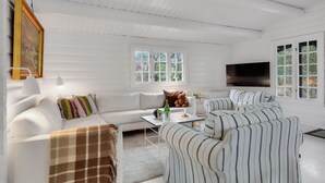 Um quarto com paredes brancas, um sofá, poltronas listradas, uma mesa de centro e uma televisão.