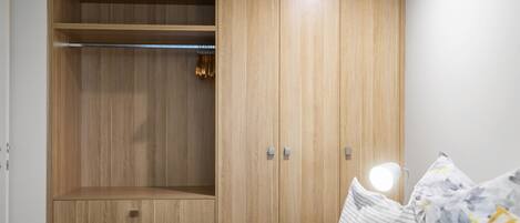 A bedroom with a wooden wardrobe, a bed with pillows, and a bedside lamp.