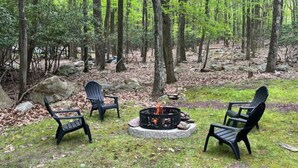 Uma área arborizada com um braseiro e três cadeiras Adirondack.