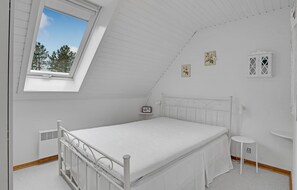 Valkoinen huone, jossa on yksi sänky, kalteva katto ja kattovalokuvio.