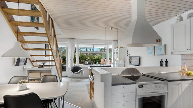 Une cuisine moderne avec des meubles blancs, un four encastré et un coin repas comprenant une table et des chaises.