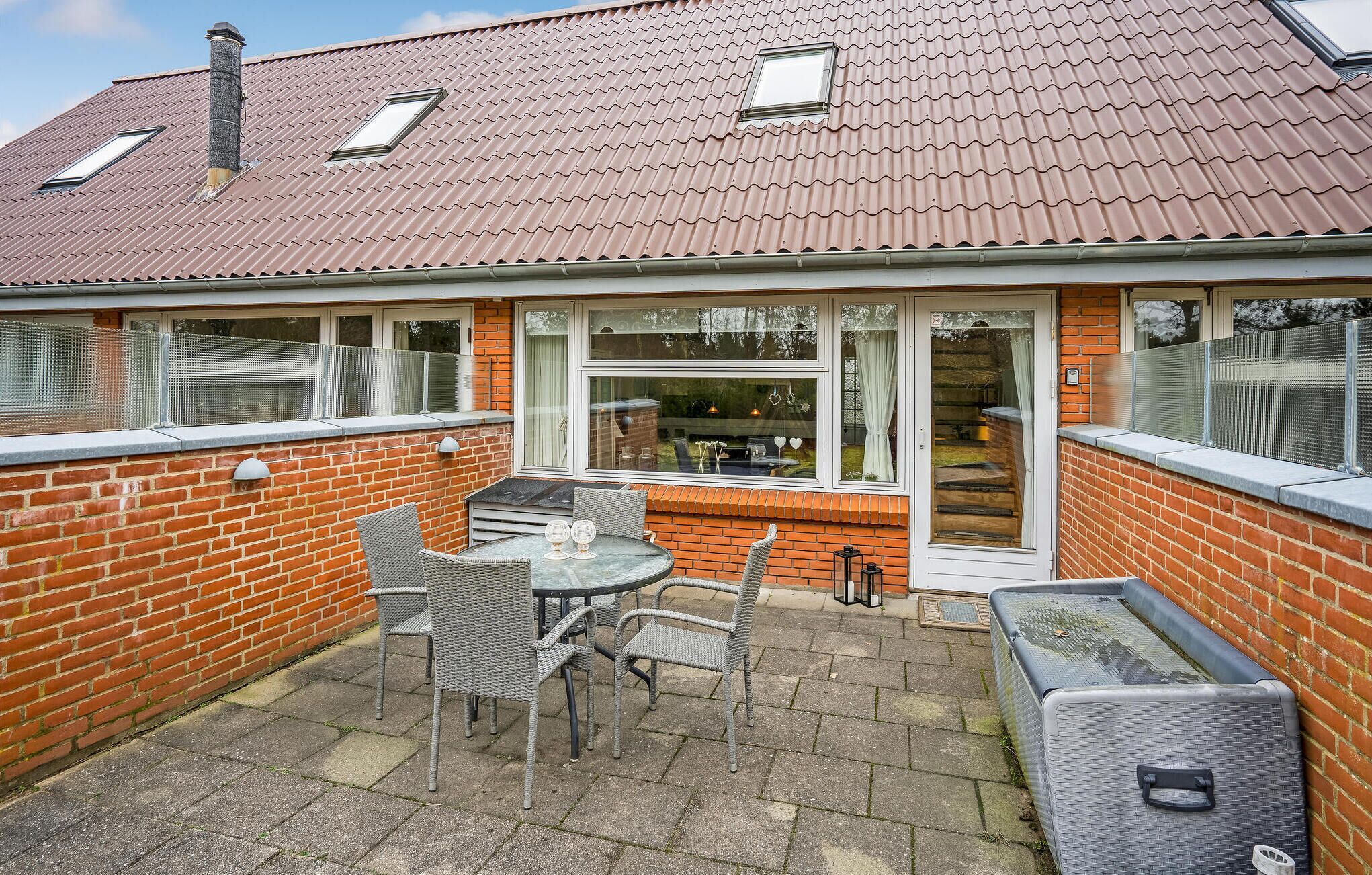 Ein Haus mit einer Terrasse, die einen Tisch, Stühle, eine Ziegelmauer und ein Fenster mit Blick auf einen Garten beinhaltet.