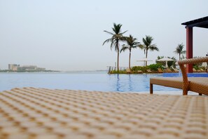Zona de piscina con sillones de descanso y palmeras.