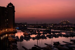 Un puerto deportivo al anochecer con barcos amarrados, un edificio destacado con cúpula y un paisaje urbano al fondo.