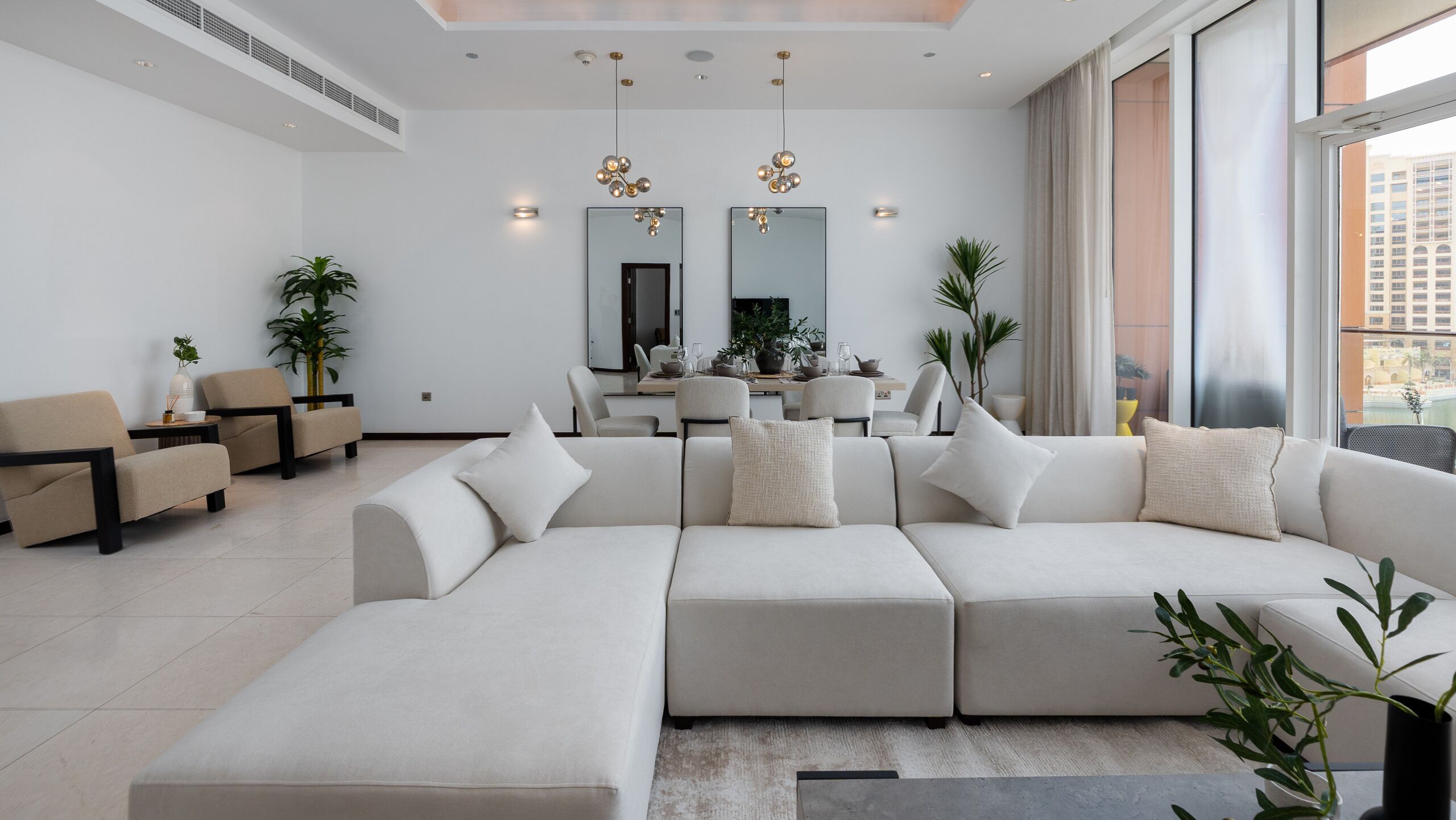 Een moderne woonkamer met een modulaire bank, een eethoek en een groot raam met uitzicht.