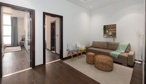 A modern living room with a brown sofa, two wicker ottomans, a small table with chairs, and a mirror on the wall.