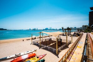 A beach with kayaks, a playground, and a city skyline in the background.