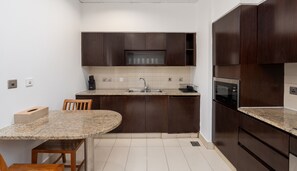 Una cocina compacta con armarios de madera oscura, encimera de granito, microondas integrado y un lavamanos.