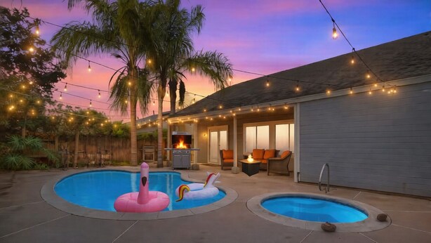 Un patio trasero con dos piscinas, mobiliario exterior, luces colgantes y una zona de barbacoa.