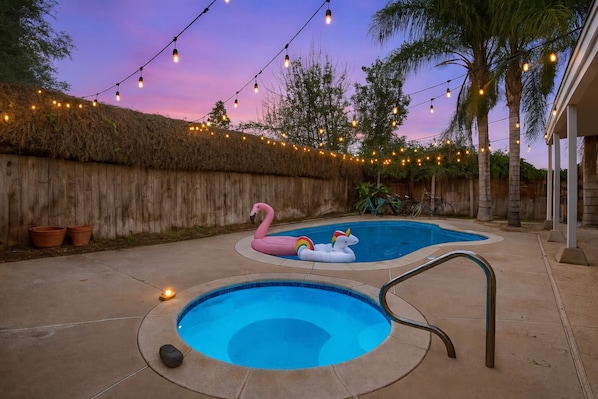 A backyard with a swimming pool, two inflatable flamingos, and string lights.