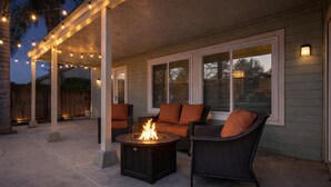 Un patio al aire libre con un brasero, muebles de mimbre e iluminación colgante.