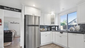 Una cocina moderna con armarios blancos, electrodomésticos de acero inoxidable y un amplio ventanal que proporciona luz natural.