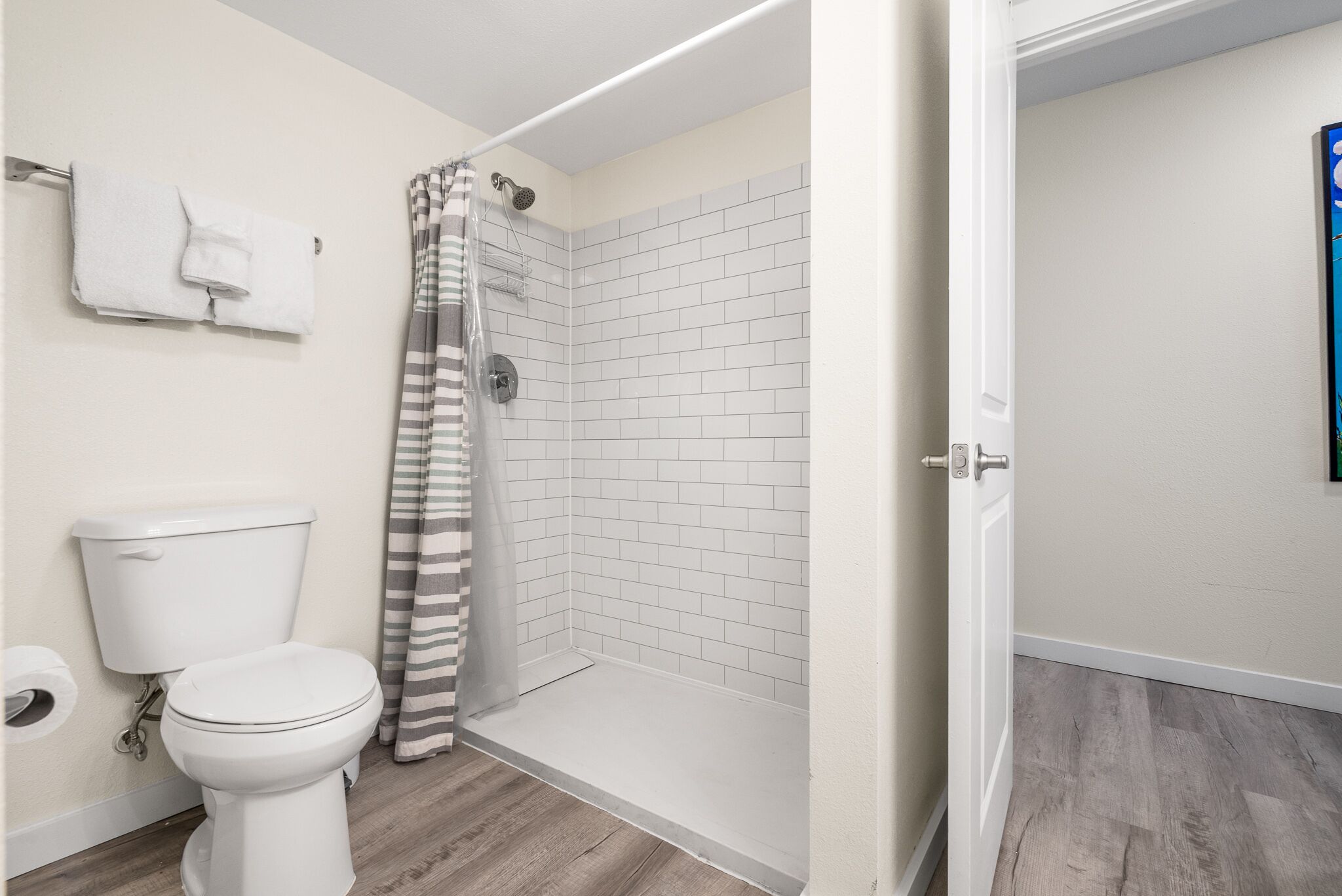 A bathroom with a toilet, a shower with a striped curtain, and a white tiled wall.